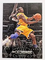 Full front view of Kobe Bryant basketball card, showing player dunking in Lakers yellow uniform with black decorative border and Panini logo.