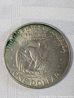 Close-up image of the obverse side of an Eisenhower 1 Dollar coin showing an eagle landing on the moon with earth in the background, and inscriptions around the edge.
