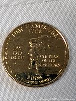 Close up photo of front side of gold plated coin showing inscriptions including New Hampshire 1788, live free or die, old man of the mountain, 2000, e pluribus unum