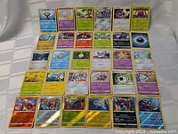 Image showing 28 Pokemon cards laid out flat including multiple holofoil cards with various Pokemon types visible like water, psychic, grass, and fire.