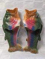 Pair of slippers shaped and painted as rainbow trout fish shown side by side on a white checkered surface.