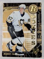 Front of 2005/06 Sidney Crosby rookie hockey card in Pittsburgh Penguins white uniform, gold 'ROOKIE' lettering and card logo.