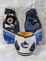 One photo showing two new fabric Vancouver Canucks beer cozy holders in plastic packaging, and one shaped cozy holder resembling a hockey jersey with gloves and team logo.