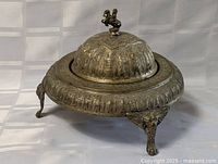 Side view of the metal antique caviar dish showing ornate embossed designs and tripodal base with decorative feet.