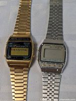 Two vintage digital Seiko wristwatches shown side by side on fabric surface, one gold-tone, one silver-tone, both with metal bands and digital displays.