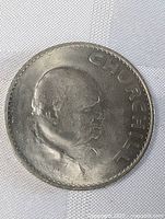 Front side of Winston Churchill English crown coin showing his profile and partial inscription.
