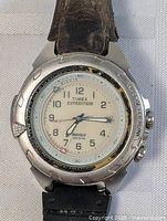 Close-up of Timex Expedition Indiglo watch face with silver-tone bezel and white dial showing numerals and minute markings.