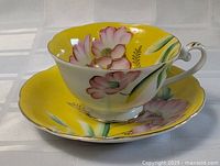 Photo of the yellow floral tea cup sitting on the matching saucer, showing floral design and cup handle detail.