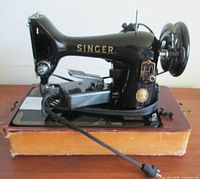 Side view of antique black Singer sewing machine on wooden base showing lettering and decals.