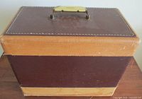 Brown two-tone hard body carrying case with cream handle and white stitching on edges, showing exterior condition and handle area.