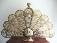Front view of folding brass fireplace screen displaying peacock clam shell design with seven panels and shell-shaped base.