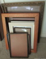 Stack of various sized picture frames leaning against a wall, showing different wood finishes including oak and gold gilt.