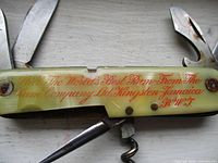 Close-up of knife handle showing red script advertising text on yellow marbled handle with some rust on screw pivot.