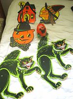 Photo showing all decorations including large black cats, pumpkin head, witch head, haunted house, and sealed pumpkin candle on white fabric.