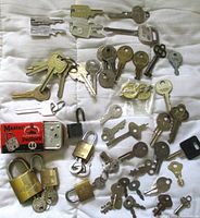 Top down view of lot showing assorted vintage padlocks and keys arranged on a cloth surface. Multiple padlocks include brand markings; keys are of various types including skeleton barrel and flat keys.