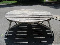 Front view of vintage round wooden slat table with collapsible aluminum legs, showing weathered wood surface and sturdy construction.