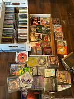 Top-down photo showing large box filled with hundreds of CD-ROM cases, and separate smaller boxes with assortment of PC game discs including Star Trek, Mario Is Missing!, Blood, Ripper, Warcraft II, Outlaws, and others.