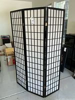 Full view of 3-panel folding room divider screen standing open, showing black wood frame with white translucent panels and brass hinges.