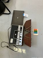 Full view of Advent tape deck with wood housing, two trapezoidal Microstatic Controls Corp. speakers, and tangled wires laid out on floor.