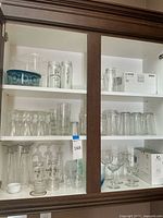 Cabinet shelves showing a variety of glassware: tall drinking glasses, small glasses, Mason jars, boxed set of wine glasses, and loose wine glasses.