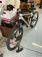 Full view of white Cannondale bike leaning beside wooden furniture with floor pump and cable lock visible