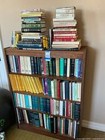 Wide shot of wooden bookshelf filled with mixed books and periodicals across three shelves and stacks on top