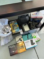 Overview of most electronic devices and accessories in the lot including Sony Walkman in packaging and Polaroid camera case.