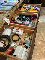 Wide shot of open drawers showing various electronic accessories, cables, tools, and household items.