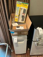 Photo showing Fellowes DM15C paper shredder with numbers around it and a box containing Premier surge protector in original packaging on top.