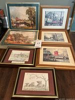 Seven framed prints arranged together showing a mix of Paris landmarks and countryside landscapes in wooden frames with mats.