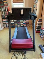 Front view of the treadmill showing the red running deck, frame, and window background.
