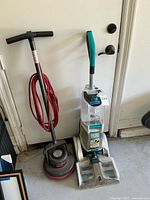 Hoover SmartWash carpet cleaner and Orleck Orbiter XL floor cleaner standing together against a door in a garage.