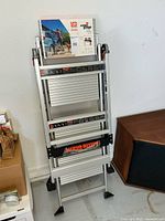 Folded aluminum ladder leaning against wall with label attached