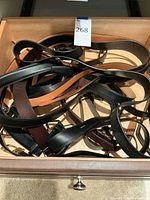 Photo of multiple men's belts in a drawer, showing various colors and buckle styles.