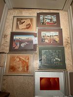 Seven framed prints arranged on floor, showing a variety of mid-century modern style artworks including landscapes and figures.