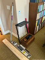Photo showing the Nitty Gritty record cleaning machine with wooden exterior and adjustable black metal laptop stand against a wall. Also visible are various cleaning accessories on the floor nearby.