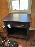 Front and side angle view of brown wooden bedside table showing drawer closed and open shelf below.