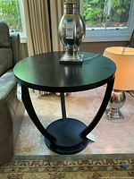Front angled view of the round black wooden pedestal side table showing smooth top surface and pedestal base with three curved supports.