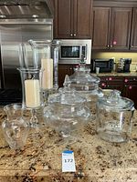 Full set on kitchen counter showing 3 large apothecary and cookie jars with lids, 2 glass candle pillars with white pillar candles, and 1 small flower vase.