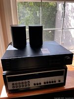 Two Sonos speakers atop Yamaha amplifier and Heathkit tuner on tabletop in front of window