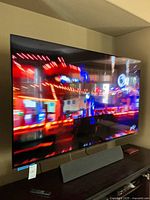 Front view of the 77-inch Sony XR TV powered on, displaying a colorful scene on its slim bezel screen, resting on a wooden console.