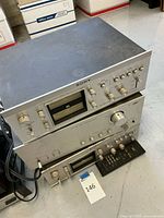 Stacked silver faceplate stereo components and black remote control on floor