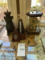 Photo of all three items: the black resin crowned bulldog figurine, Wittner pyramid metronome open to show pendulum, and Kundo quartz clock with wooden octagonal case.
