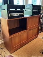 Wooden entertainment center cabinet with open shelf space, two lower cabinet doors, and medium wood tone finish. Electronics resting on top are not included in the lot.