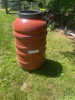 Red MiRain barrel standing on grass outdoors with woodpile in background.