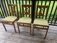Front view of three vintage wooden folding chairs showing cushioned seats and decorative backs.
