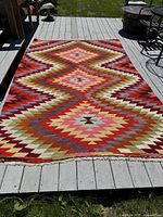 Full view of the colorful geometric patterned Kilim rug laid flat on an outdoor deck showing its overall size and condition.