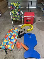 Full lot with chair, cooler, boogie board, pool floats, ball, and pool belt all displayed on concrete floor