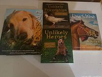 Photo displaying all four books laid flat with covers visible: Dogs 24/7, Unlikely Friendships, Unlikely Heroes, King of the Wind