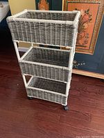Front angled view of the three-tier wicker basket shelving unit showing woven baskets and caster wheels.